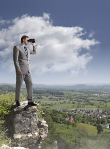 Businessman standing at the edge of a cliff looking through binoculars concept for job search, business vision or looking to the future